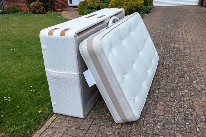 two workers loading a mattress onto a truck for disposal